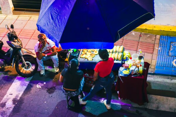 Colorful street food scene featuring vendors under a vibrant umbrella in Popayán, Cauca, Colombia, with various dishes on display.