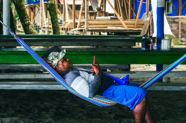 Relaxing in a colorful hammock, a man checks his phone at Chucheros Beach, Uramba, Bahía Málaga, Valle del Cauca, Colombia.