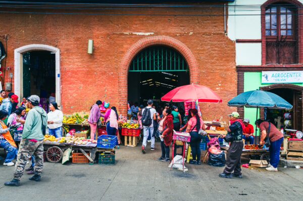Vibrant market scene in Cauca, Colombia, featuring vendors under colorful umbrellas and baskets of fresh produce.
