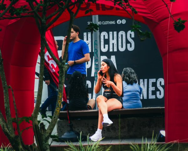 Young woman sitting on a bench while eating, framed by a vibrant red arch in Parque Caldas, Popayán, Cauca, Colombia.