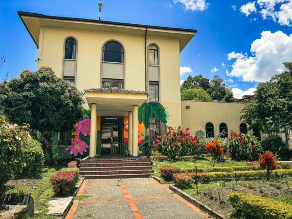 Natural History Museum features colorful murals and lush gardens in Popayán, Cauca, Colombia, under a vibrant blue sky.