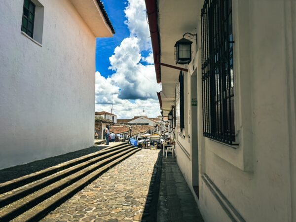 Bright blue skies with fluffy clouds overlook a cobblestone street lined with whitewashed buildings in Popayan, Cauca, Colombia.