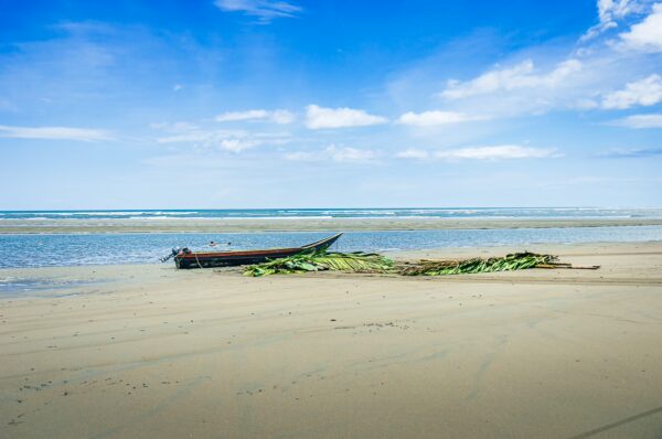 Tranquil shoreline with a fishing boat resting on sandy beach, bright blue sky, and calm waves in La Barra, Valle del Cauca, Colombia.