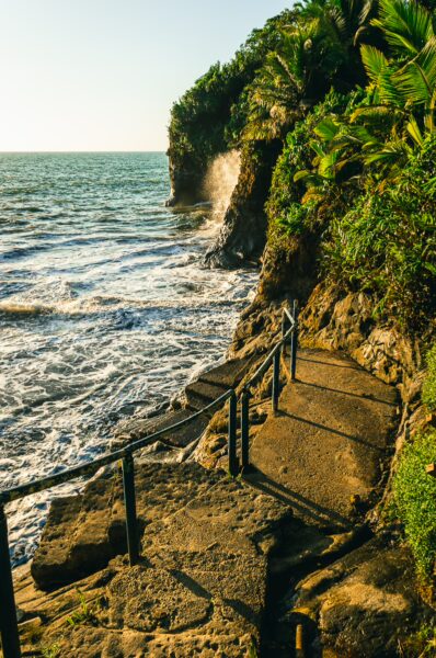 Winding stone steps lead down to the waves at Ladrilleros, surrounded by lush greenery and coastal cliffs in Valle del Cauca, Colombia.