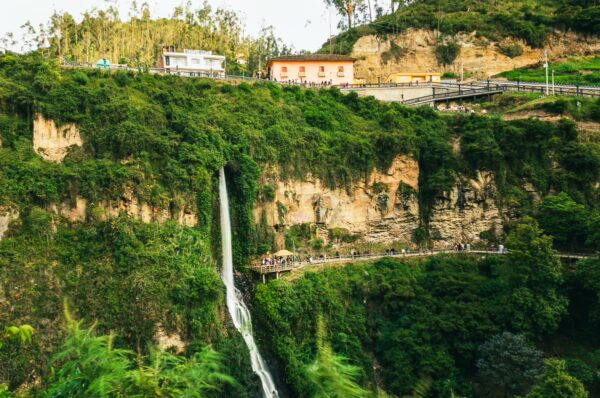 A cascading waterfall flows down lush green cliffs near the buildings of Las Lajas, Nariño, Colombia.
