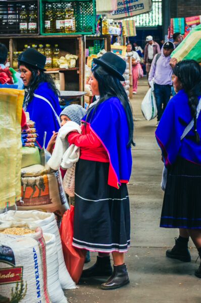 Colorful market scene in Cauca, Colombia, featuring women in traditional dress with vibrant blue capes and dark skirts amidst local goods.