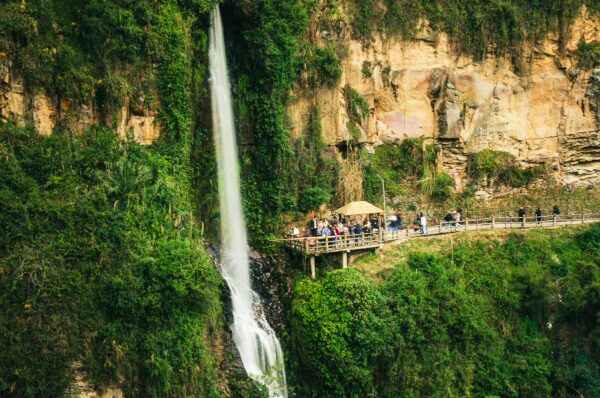 Las Lajas features a stunning waterfall cascading down a lush green cliff, with visitors admiring the view from a nearby observation deck.
