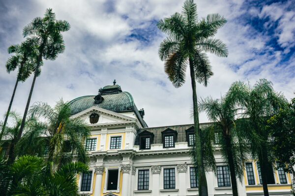 Plaza de Cayzedo in Cali features elegant architecture framed by tall palm trees under a cloudy sky, creating a vibrant scene.