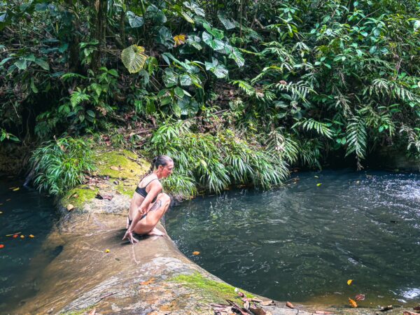 Calm waters of the Tres Marias River flow through lush greenery, with a person relaxing by the water's edge in Valle del Cauca, Colombia.
