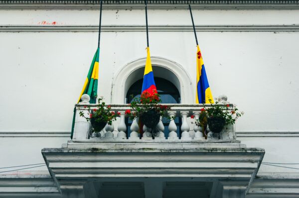 Colorful flags adorn a charming balcony with vibrant flowers, set against the white walls of a building in Popayán, Cauca, Colombia.
