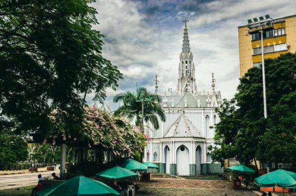 La Ermita's iconic white façade contrasts with the lush greenery and vibrant umbrellas in the lively Cali, Valle del Cauca.