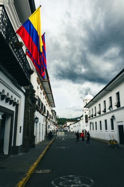 Colorful flags adorn the white colonial buildings lining the street in Popayán, Cauca, Colombia, under a dramatic sky.