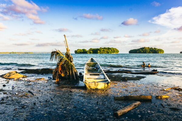 Sunlight reflects on the water at Juanchaco, Valle del Cauca, with a boat and palm tree on the shore and lush islands in the distance.