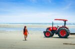 Bright red tractor on the sandy beach in La Barra, Valle del Cauca, Colombia, with a woman walking towards the ocean waves.