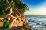A woman sits on a rocky ledge, gazing at the sunset over the ocean in Ladrilleros, Valle del Cauca, Colombia.