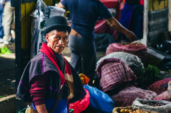 Vibrant market scene in Cauca, Colombia, featuring a man in traditional attire, surrounded by colorful produce and textiles.