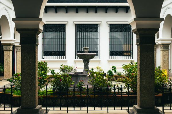 Stone fountain surrounded by lush greenery in a courtyard framed by elegant arches in Popayán, Cauca, Colombia.
