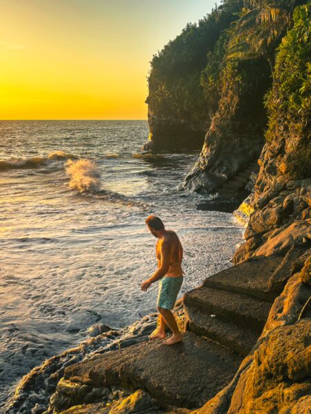 Golden sunset over Ladrilleros, Valle del Cauca, Colombia, with a figure standing on rocky shores beside gentle waves.