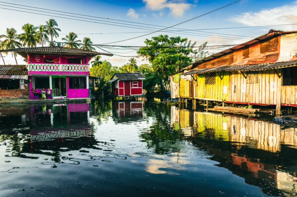 Colorful houses reflected in calm waters of Juanchaco, Valle del Cauca, Colombia, surrounded by lush palm trees and blue skies.