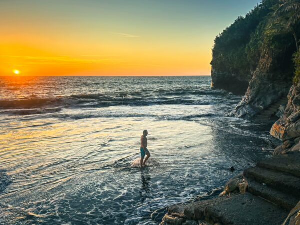 Golden sunset casts warm hues over the waves at Ladrilleros, Valle del Cauca, Colombia, while a figure walks along the shore.