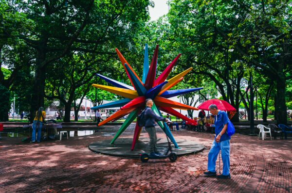 Colorful star sculpture among lush green trees in Parque La Retreta, Cali, Valle del Cauca, Colombia, with visitors enjoying the space.