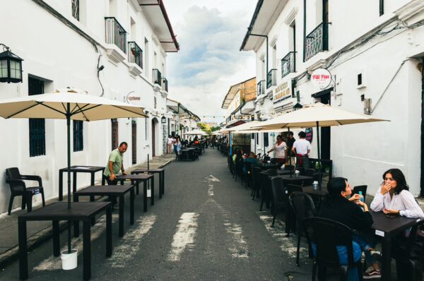 Colorful street scene in Popayán, Cauca, Colombia, featuring outdoor cafes, white buildings, and a lively atmosphere.