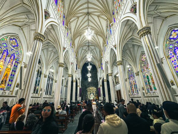 Stunning stained glass windows illuminate the elegant interior of Las Lajas Sanctuary, filled with visitors in Narino, Colombia.