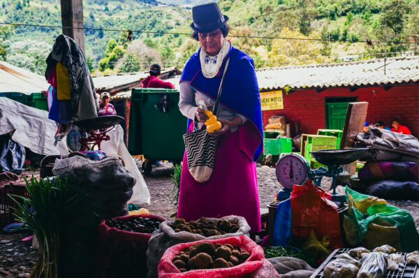 Colorful market scene in Cauca, Colombia, featuring a vendor in traditional attire selling fresh produce amidst vibrant sacks.