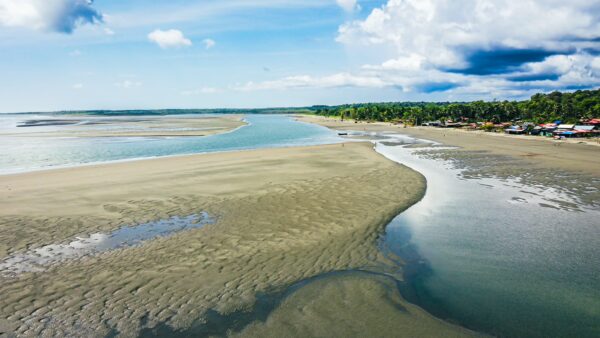 Sandy riverbanks and blue waters contrast with lush greenery along La Barra, Valle del Cauca, Colombia, under a bright sky.