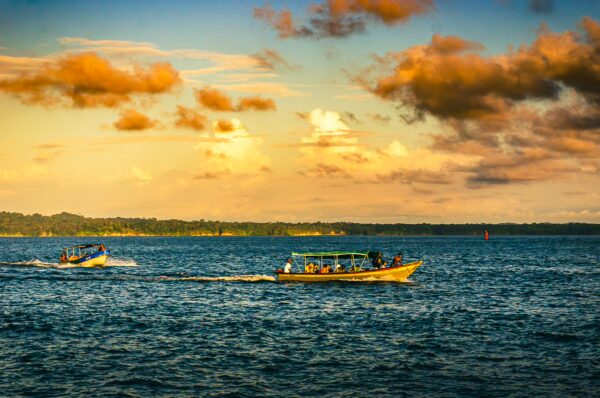 Colorful boats navigate the sparkling waters of Juanchaco, Valle del Cauca, Colombia, under a vibrant sunset sky.