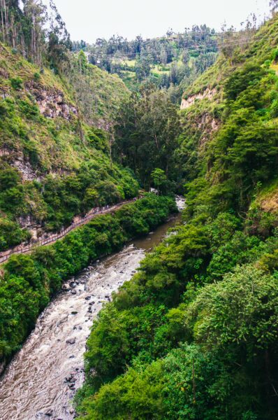 Lush greenery frames the winding river in Las Lajas, Nariño, Colombia, showcasing vibrant foliage and rocky banks.