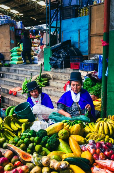 Vibrant market scene in Cauca, Colombia, featuring two women in traditional dress surrounded by colorful fruits and vegetables.