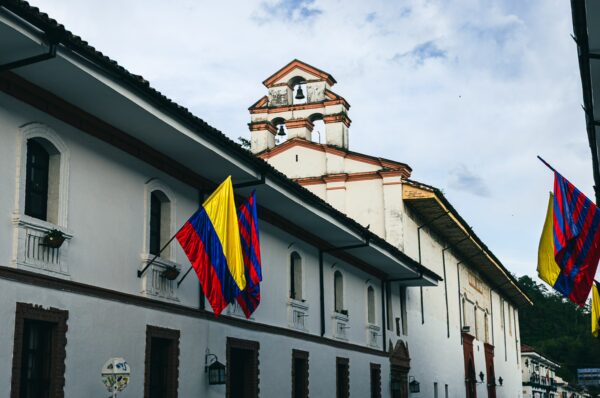 Colorful Colombian flags hang outside the historic Nuestra Señora del Carmen church in Popayán, Cauca, against a cloudy sky.