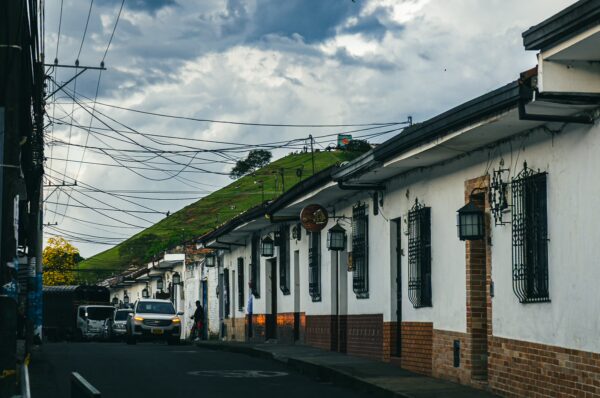 Charming white-walled houses line the street in Popayán, Cauca, Colombia, framed by a dramatic sky and green hills in the distance.