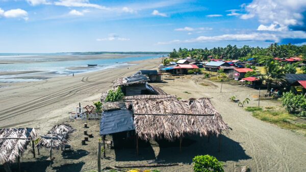Thatched-roof huts line the sandy beach of La Barra, Valle del Cauca, Colombia, under a vibrant blue sky.