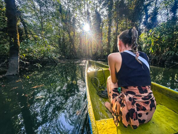 Serene scene in Ladrilleros, with a woman sitting in a yellow canoe surrounded by lush greenery reflecting on calm waters.