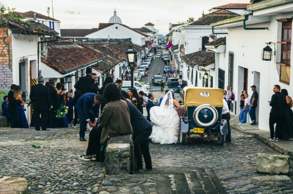 Historic cobblestone street in Popayán, Colombia, bustling with a wedding party and classic car against white colonial buildings.