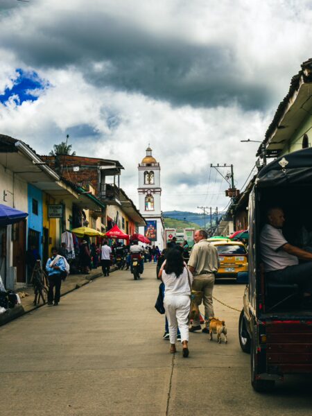 Vibrant street scene in Cauca, Colombia, featuring colorful shops, cloudy skies, and people strolling alongside a clock tower.