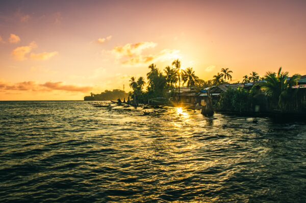 Golden sunset reflecting on the water, with palm trees silhouetted along the shoreline in Juanchaco, Valle del Cauca, Colombia.