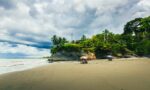Golden sand stretches along Ladrilleros beach, dotted with colorful umbrellas and lush greenery under a dramatic sky in Valle del Cauca, Colombia.
