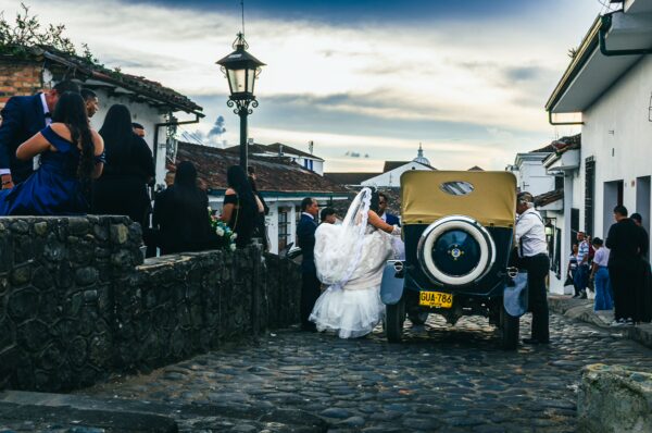 Elegant bride in a white dress near a vintage car, set against cobblestone streets and colonial buildings in Popayán, Cauca.