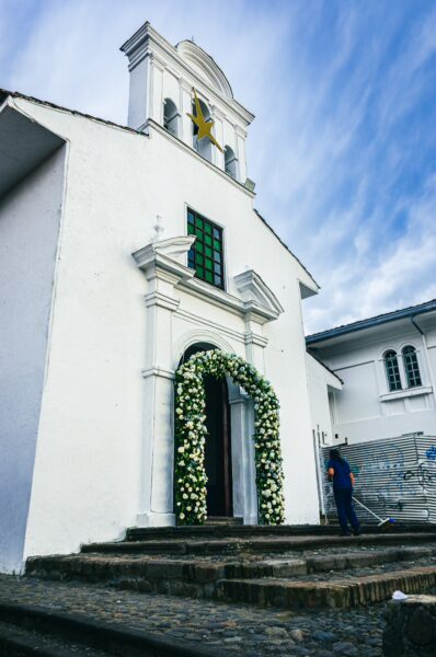Ermita de Jesús features a white facade adorned with flowers, a green window, and a star atop the bell tower in Popayán, Cauca.