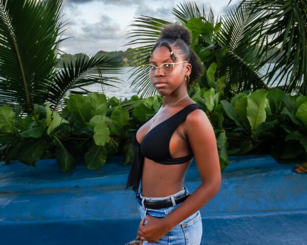 A young woman in a black top stands confidently by lush green plants near the water in Juanchaco, Valle del Cauca, Colombia.