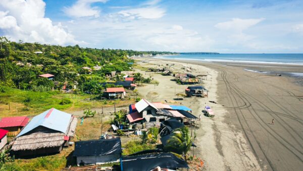 Colorful roofs dot the sandy shores of La Barra in Valle del Cauca, Colombia, with lush greenery and a serene beach backdrop.