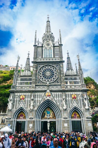 Stunning architecture of Las Lajas Sanctuary in Nariño, Colombia, crowds gather under a blue sky, highlighting its intricate details.