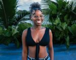 Smiling young woman in a black top stands against lush greenery near Juanchaco, Valle del Cauca, Colombia.