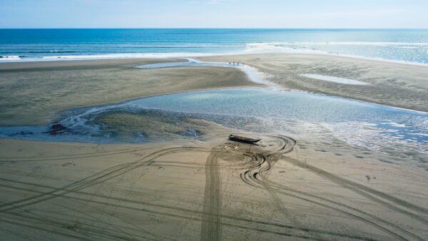 Tranquil beach scene in La Barra, Valle del Cauca, Colombia, featuring a lone boat on the sand and shallow water pools.