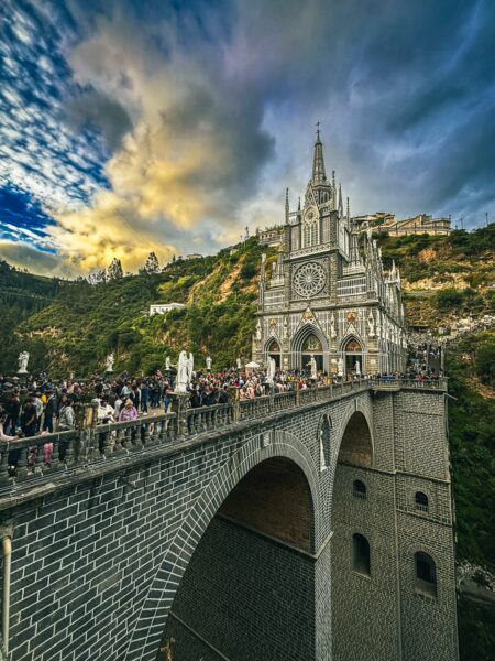 Majestic Las Lajas Sanctuary perched atop a striking archway, surrounded by lush greenery and a dramatic sky in Narino, Colombia.