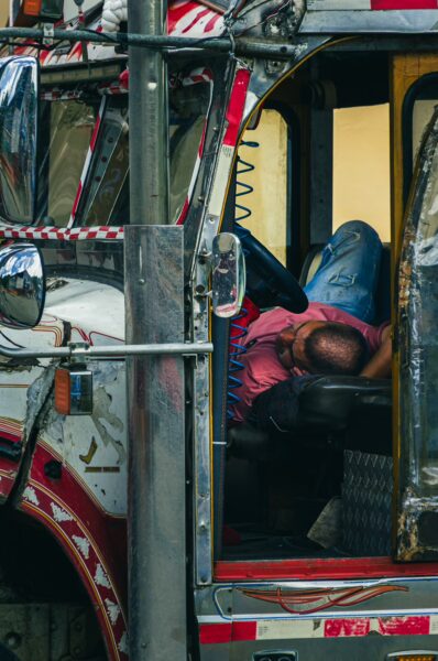 Vibrant red and silver truck parked in Cauca, Colombia, with a driver resting on the wheel, showcasing local transportation culture.