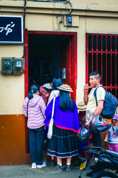Locals gather at a doorway in Cauca, Colombia, characterized by vibrant clothing and a lively street scene.